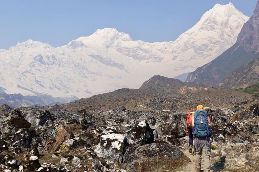 Trekkers hiking through rocky moraine terrain with snow-capped Himalayan peaks in background